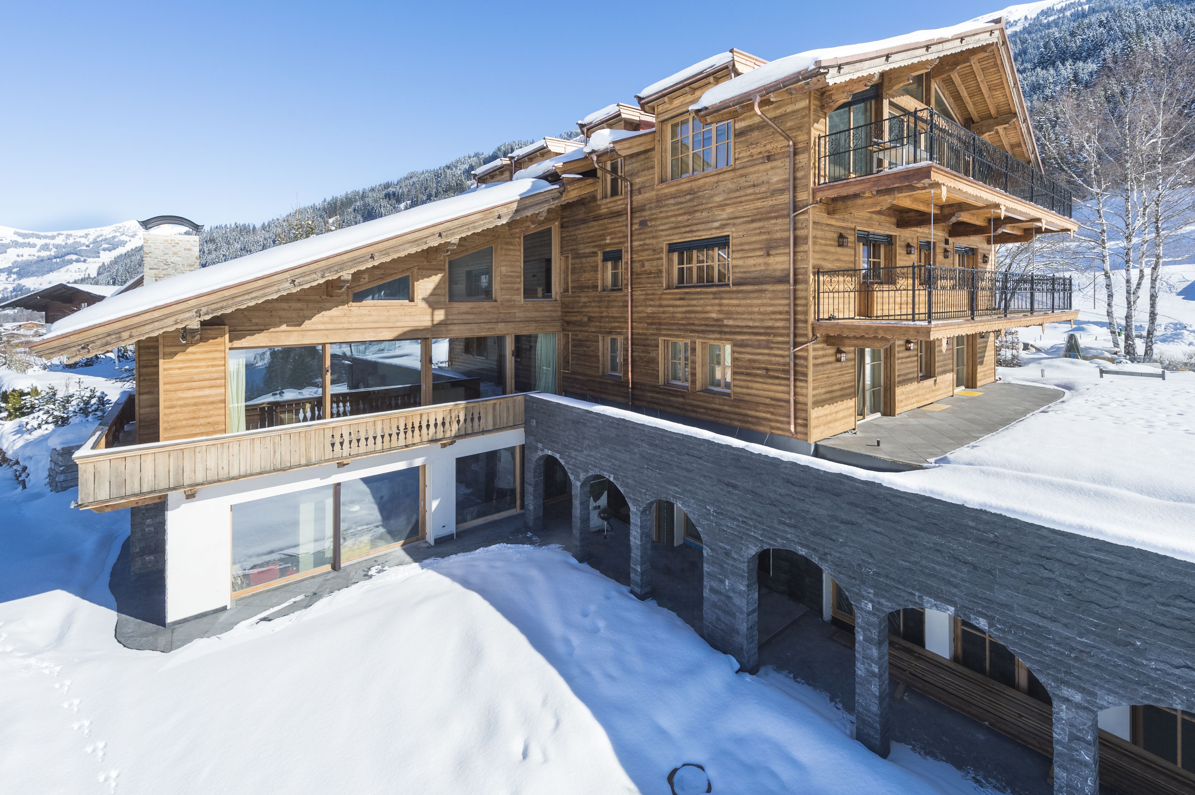 A multi-story wooden chalet with balconies, large windows, and a stone bridge leading to the entrance.