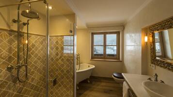 Un bagno con doccia vetro, vasca freestanding, lavabo e finestra vista montagne innevate.