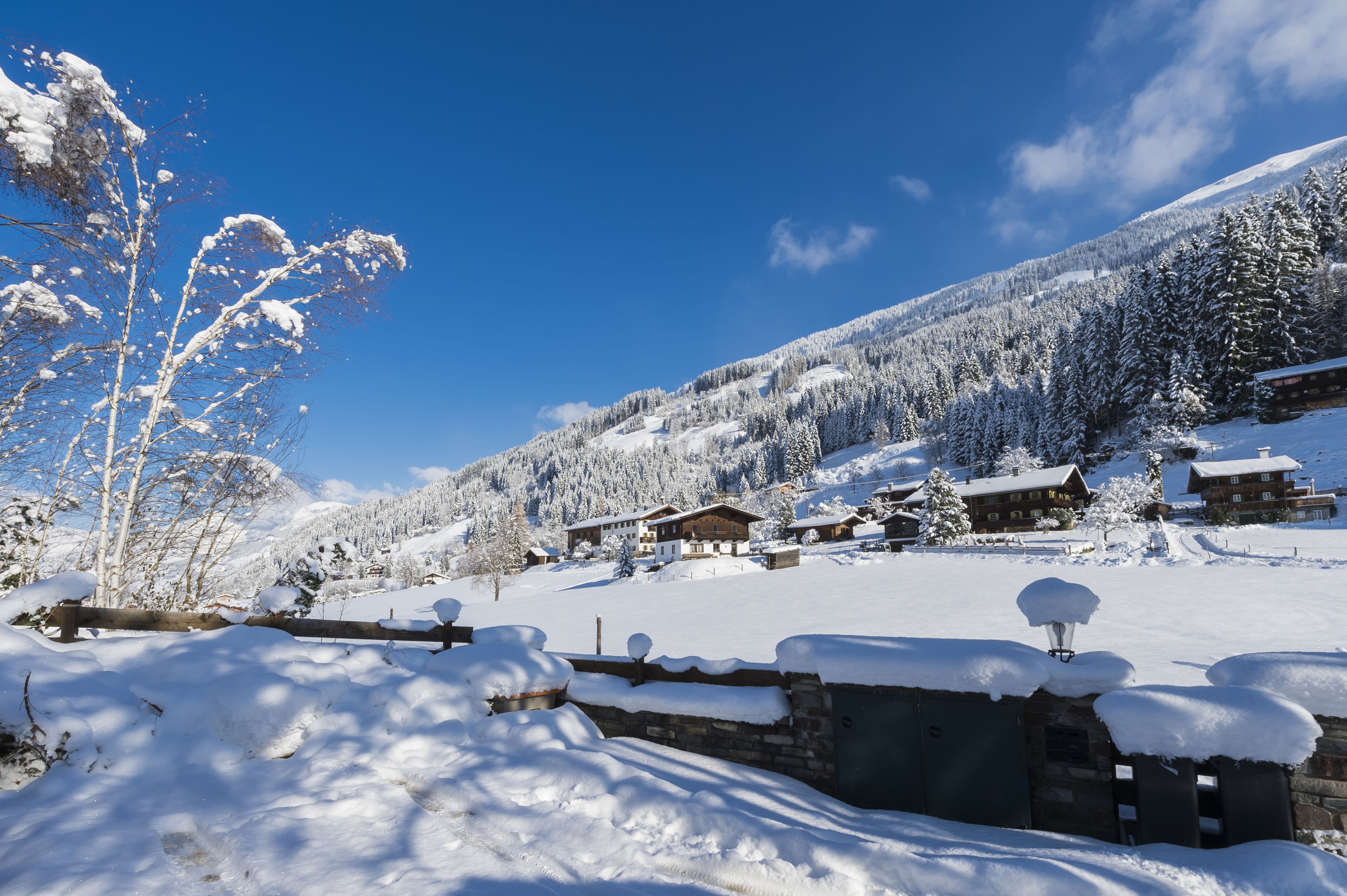 Un village enneigé, avec des maisons en bois et une chaîne de montagnes en arrière-plan.