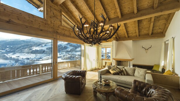 Een ruime woonkamer met een groot raam dat uitkijkt op een besneeerd landschap, een houten plafond en een kroonluchter.