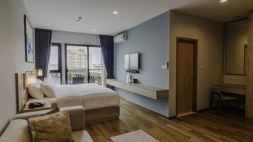 A modern hotel room with a bed, a sofa, a desk, and a balcony with a view of the city.