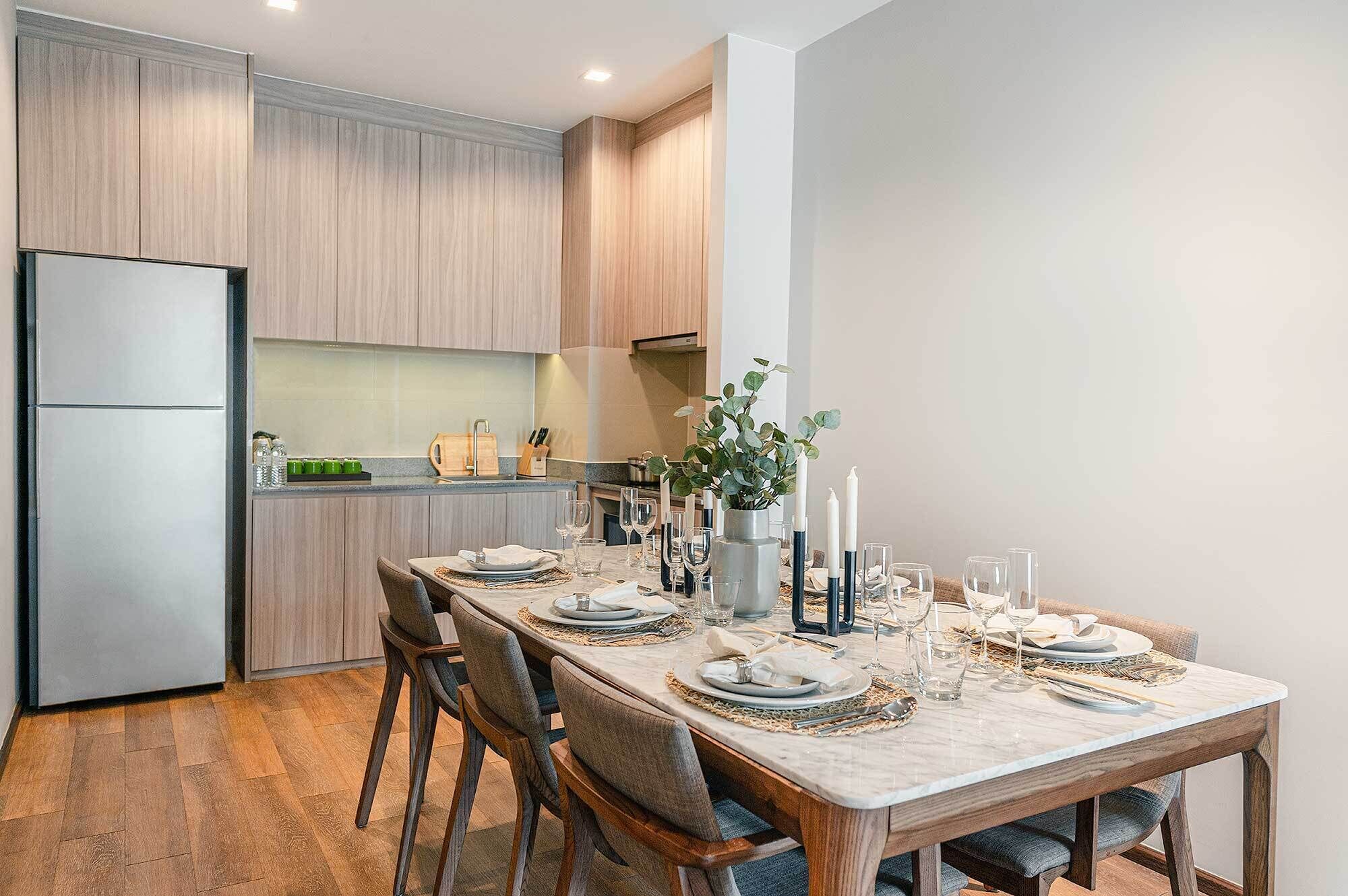 Une cuisine moderne avec des meubles en bois, un four encastré et un coin repas aménagé pour six personnes, avec une table et des chaises en marbre.