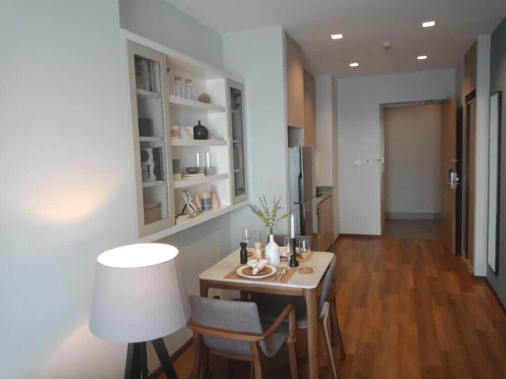 Un comedor con una mesa lista para dos personas, una lámpara y una estantería con utensilios de cocina.