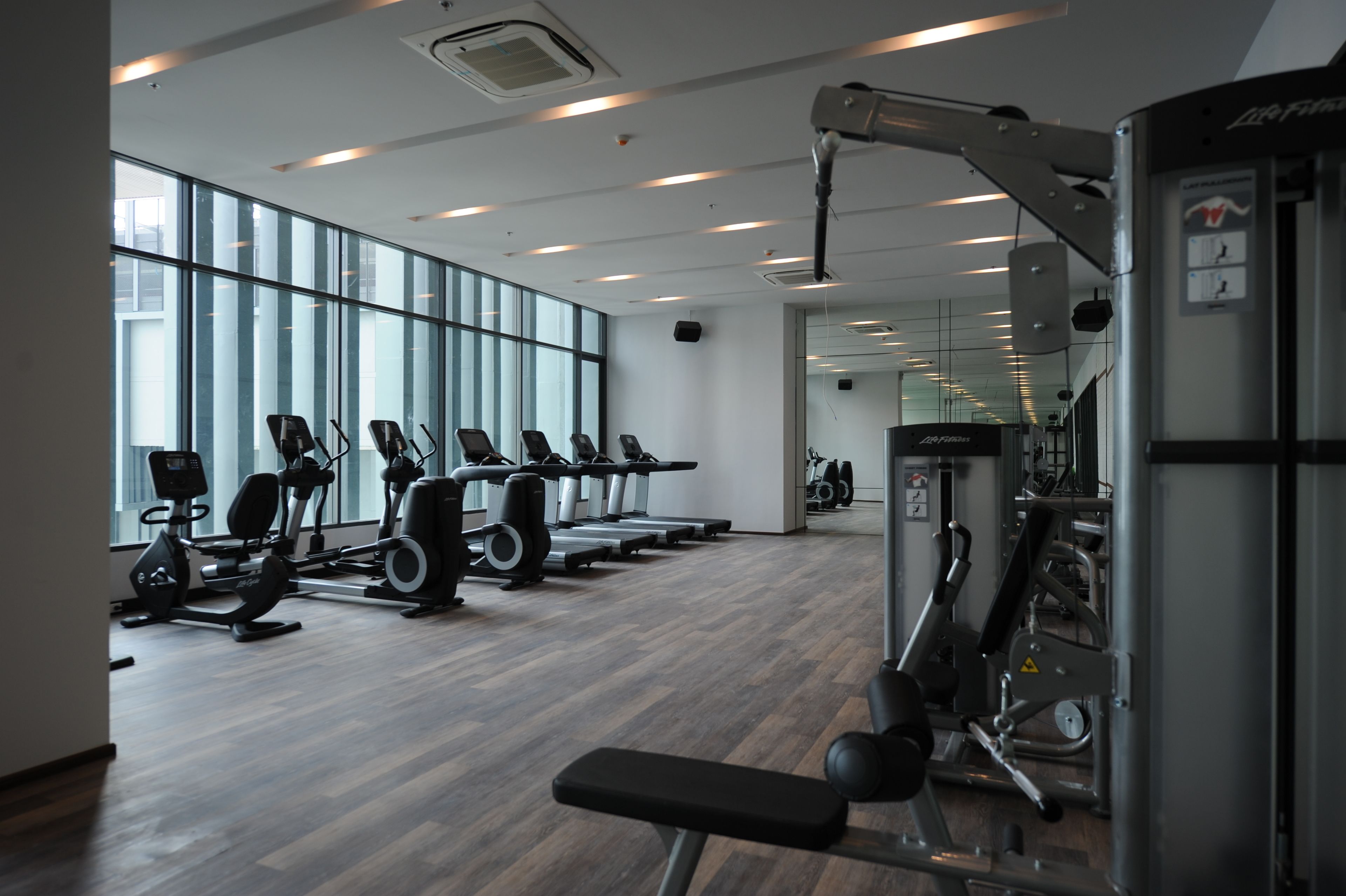 A modern gym with exercise equipment, large windows, and a clean, organized layout.