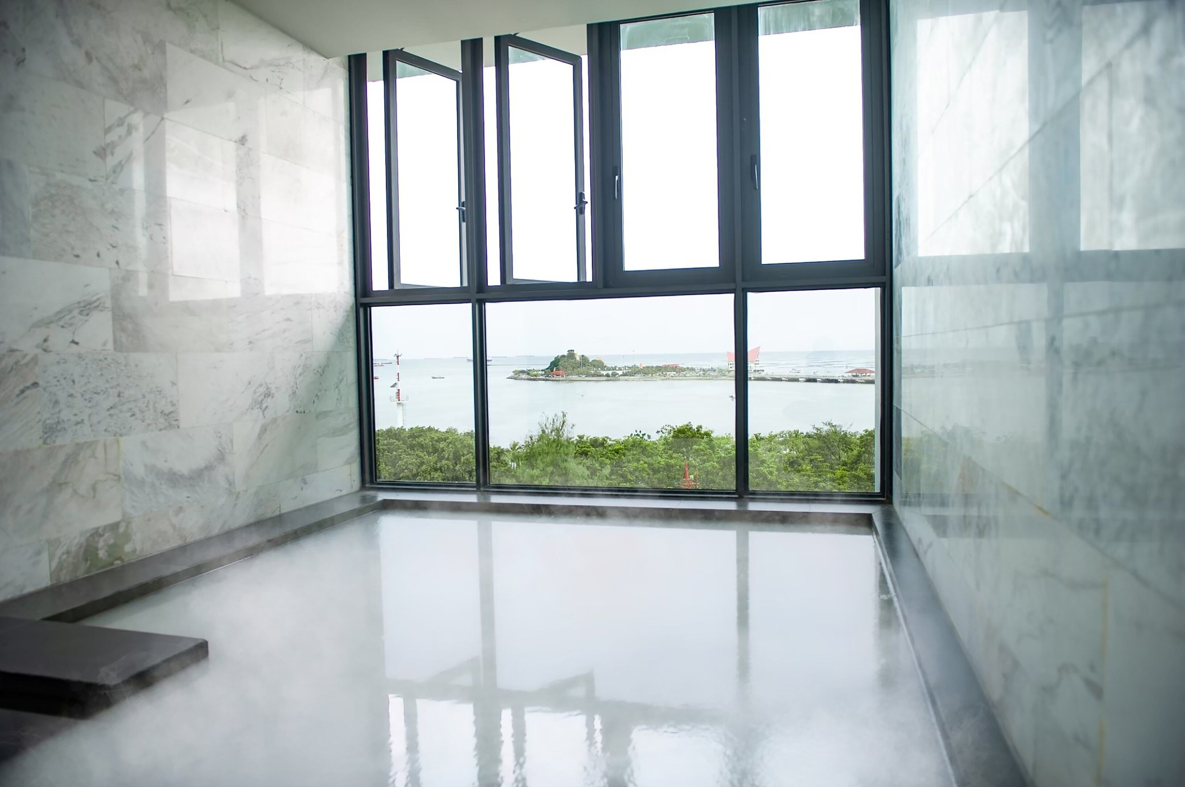 A modern room with large windows, a marble floor, and a view of a distant island.