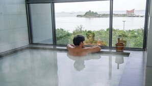 A man relaxing in a glass-bottomed pool with a view of a body of water and greenery. - Oakwood hotel & Residence Sri Racha (Si Racha)