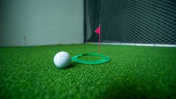 A golf ball on artificial grass near a green flag.