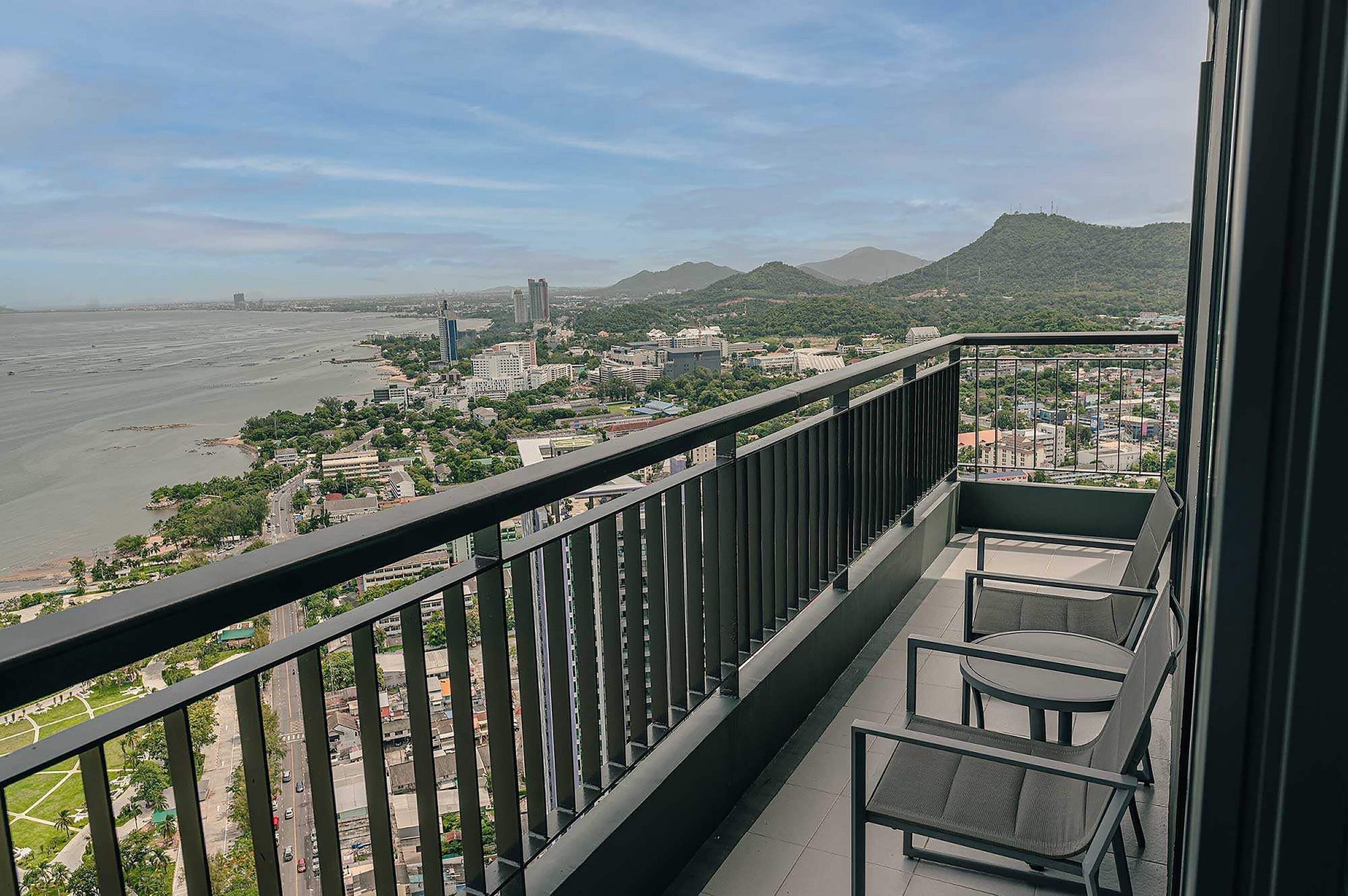 Un balcón con vista a una playa y al paisaje urbano, incluyendo edificios y montañas.