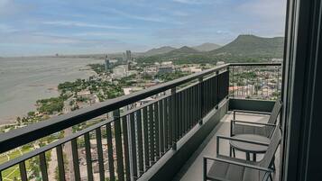 Un balcón con vista a una playa y al paisaje urbano, incluyendo edificios y montañas.