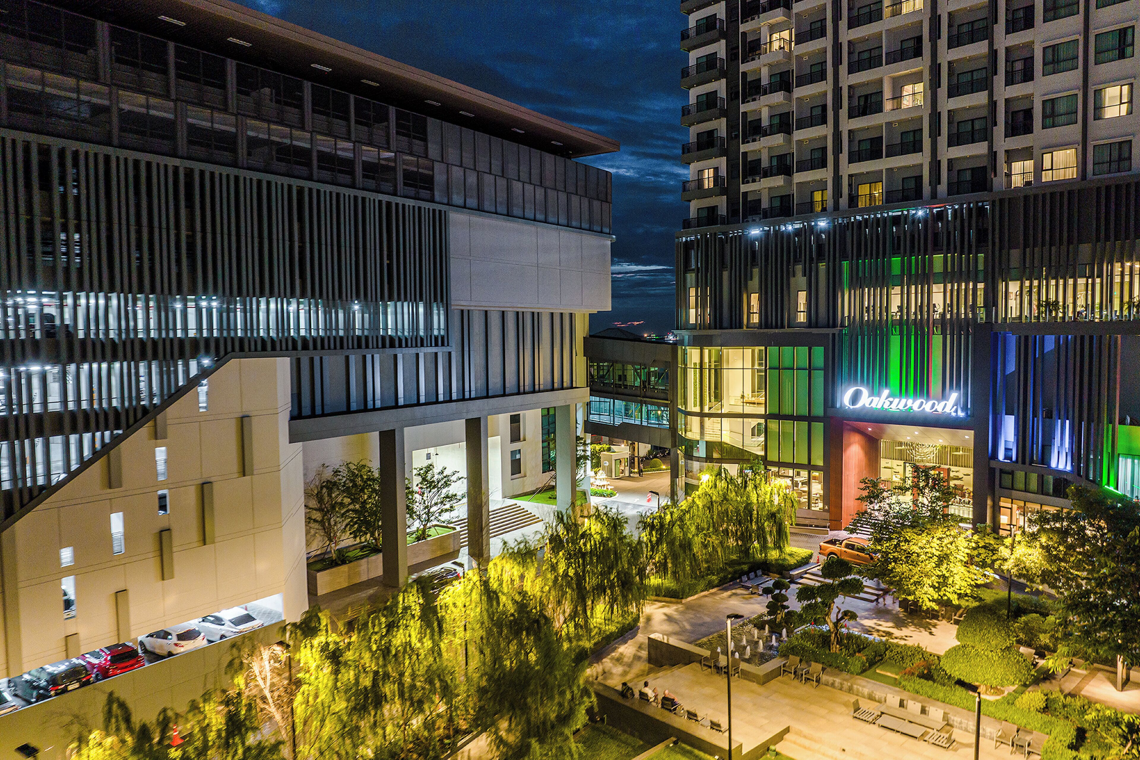 A modern hotel with a prominent 'Oakwood' sign, outdoor seating, and a well-lit parking area.