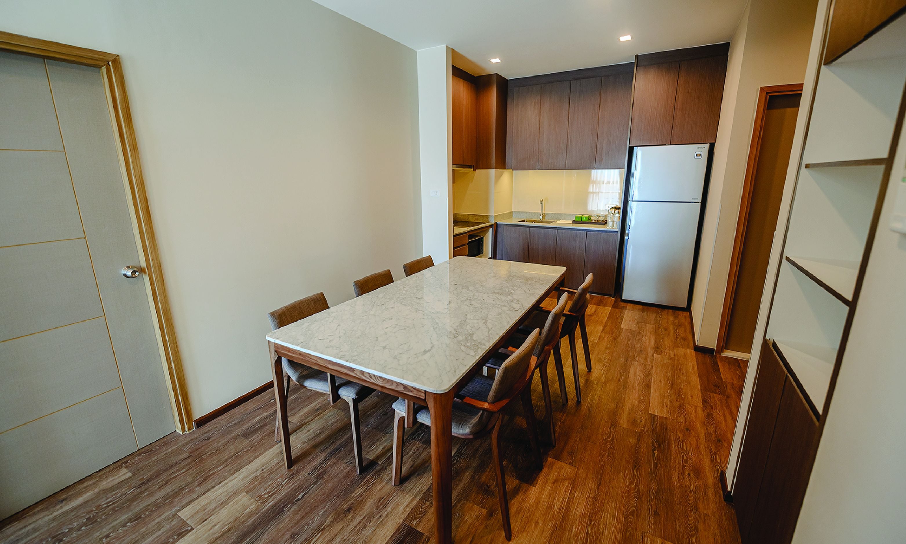 A compact kitchen with wooden cabinets, a marble countertop, and a built-in refrigerator.