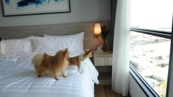 Een hotelkamer met een bed, een nachtkastje met een lamp en een raam met uitzicht op gebouwen.