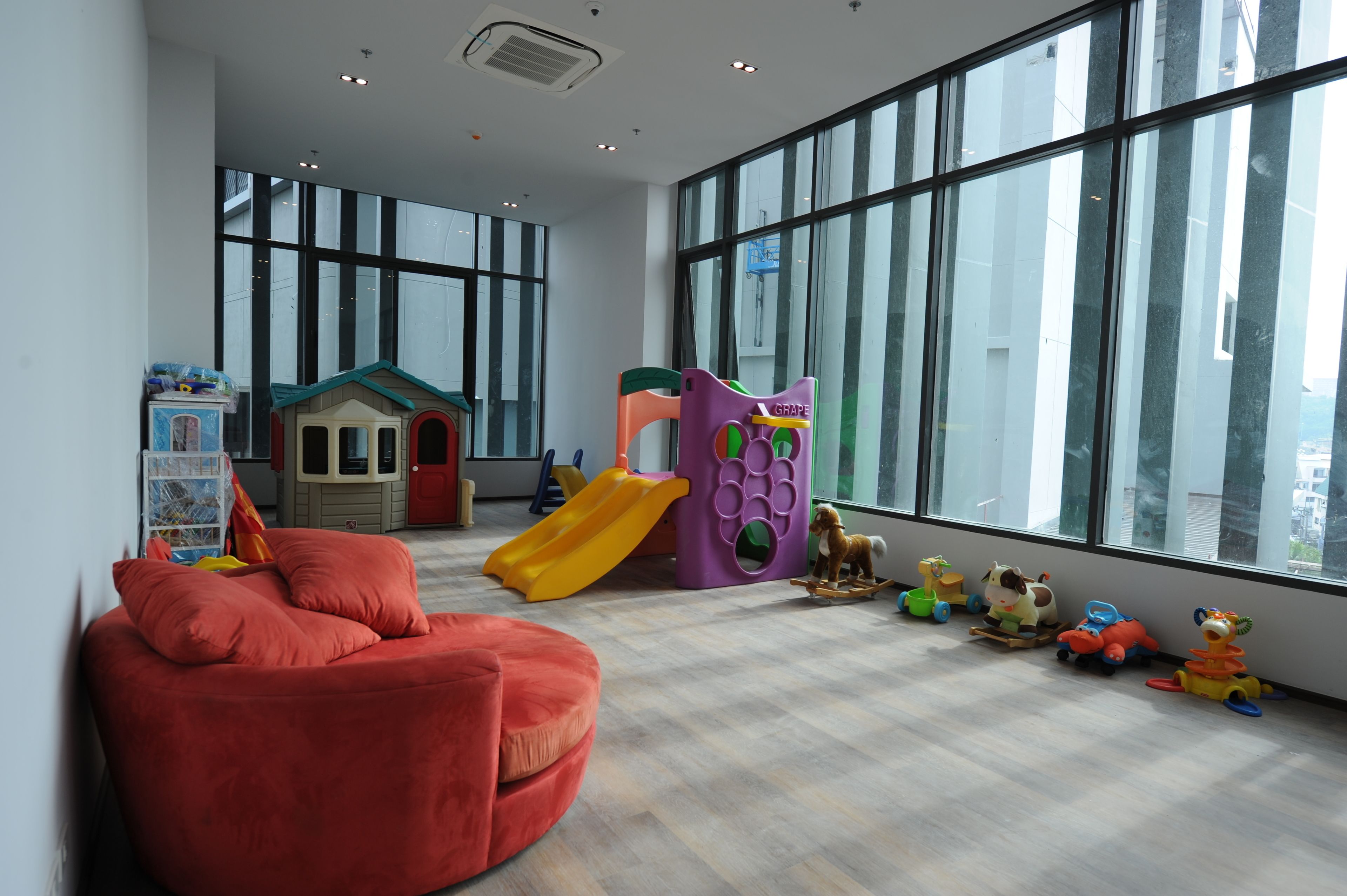 A spacious room with large windows, a play area with a slide, and a red chair.
