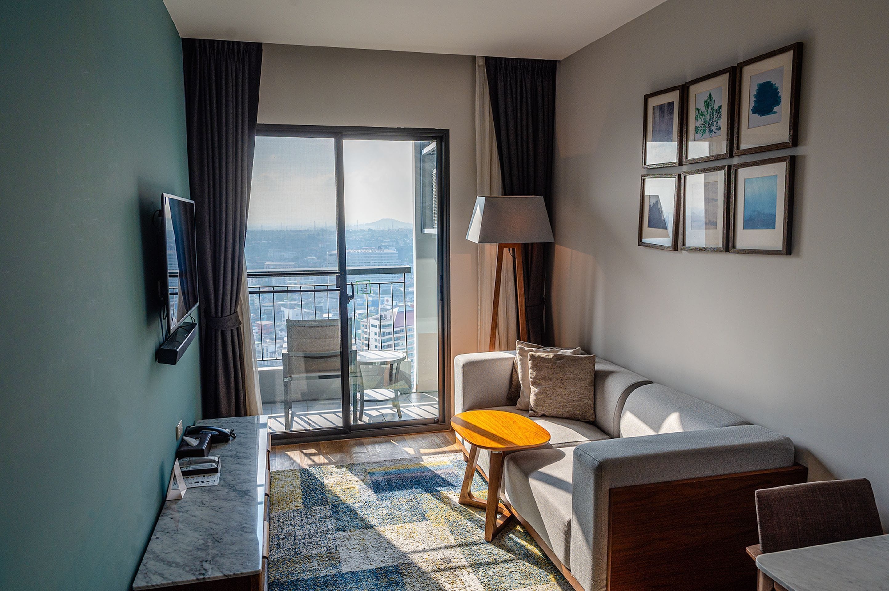 A hotel room with a balcony, a sofa, a small table, a lamp, and framed pictures on the wall.