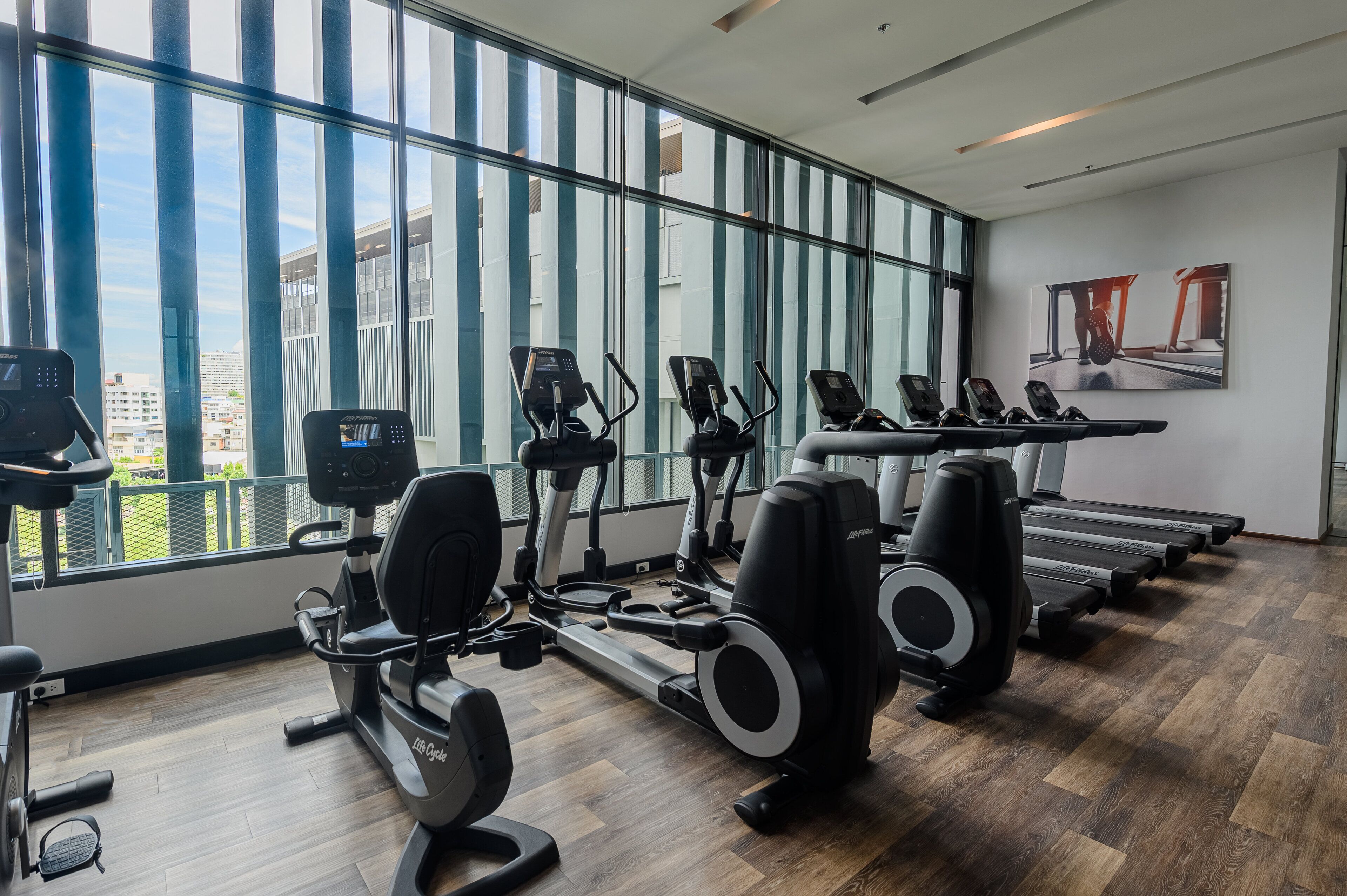 Un gimnasio moderno con máquinas de cardio, equipo de pesas y grandes ventanales con vistas a la ciudad.