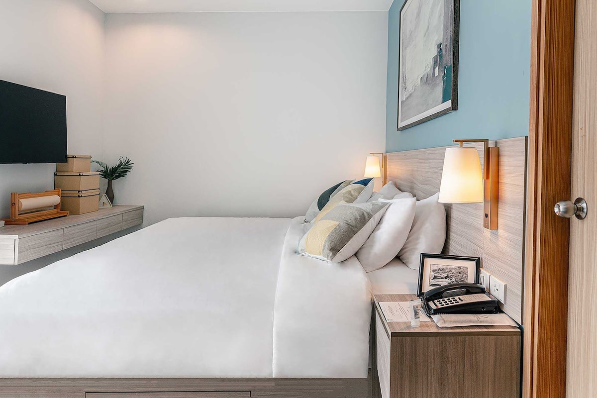 Ein Hotelzimmer mit einem großen Bett, Nachttischlampen, einem Flachbildfernseher, einem Holznachttisch und einem gerahmten Bild an der Wand.