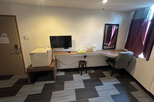 A small, modern room with a desk, chair, and a flat-screen TV. There is a window with curtains, a door, and a small stool. - Hotel Midtown Villa (Kuala Lumpur)