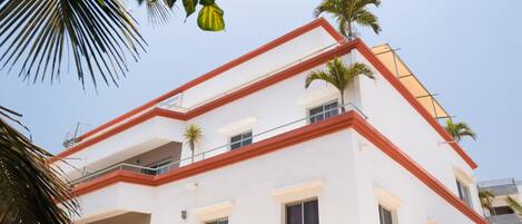 A multi-story building with a white facade and red accents, featuring balconies and windows.