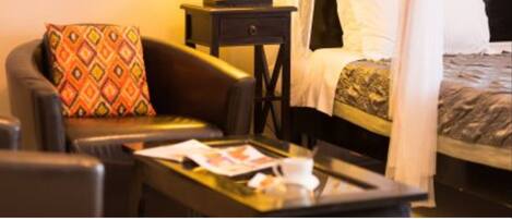 A hotel room with a bed, a bedside table with a lamp, a sofa with a patterned cushion, and a glass coffee table.