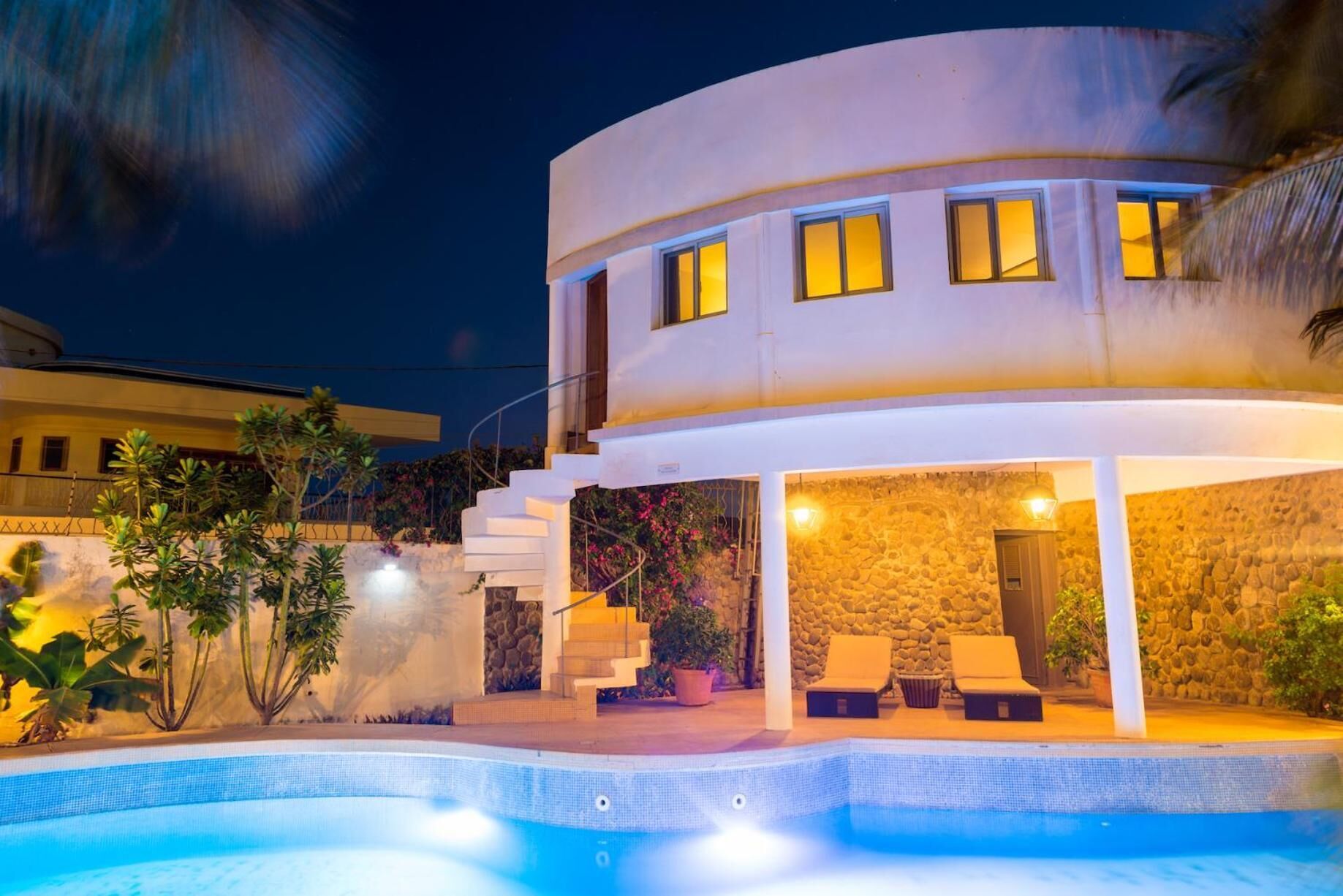 Una casa moderna de dos pisos con piscina, muros de piedra y una escalera que conduce al nivel superior.