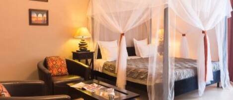 A four-poster bed with a canopy, a bedside table with a lamp, a chair, and a small table with a magazine.