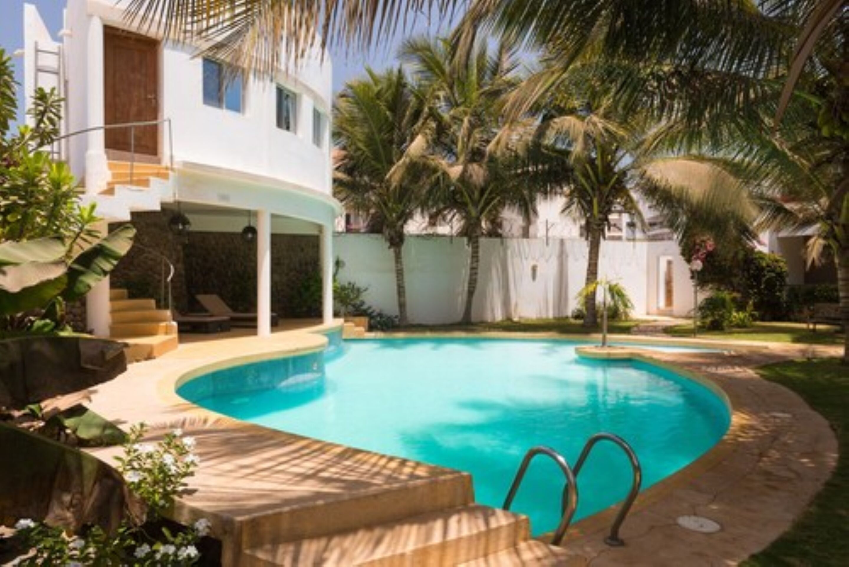 Una casa moderna con piscina, rodeada de palmeras y un jardín cuidado.
