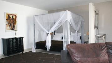 Quarto com cama de dossel, mesa de cabeceira, cômoda e poltrona de couro marrom.
