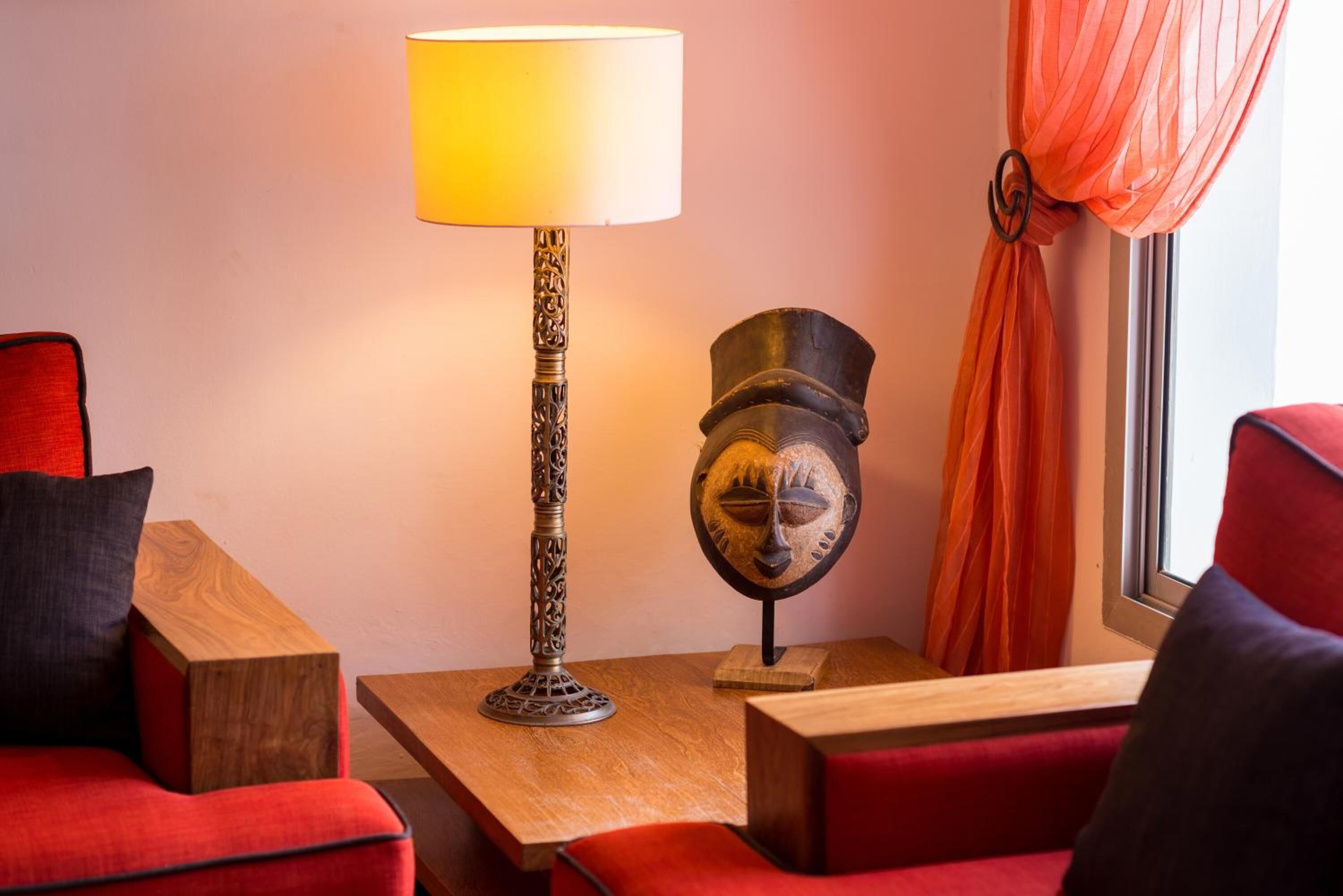 Une pièce avec un canapé rouge, une table d’appoint en bois, une lampe et un objet décoratif posé sur la table.