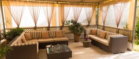 A covered outdoor seating area with cushioned sofas, a coffee table, and potted plants.