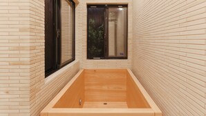 Een spa-ruimte met een houten bad, een raam met uitzicht op groen en een bakstenen muur.