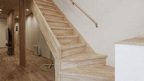 Een houten trap met een leuning, een vlakke balkenplafond en een witte muur.
