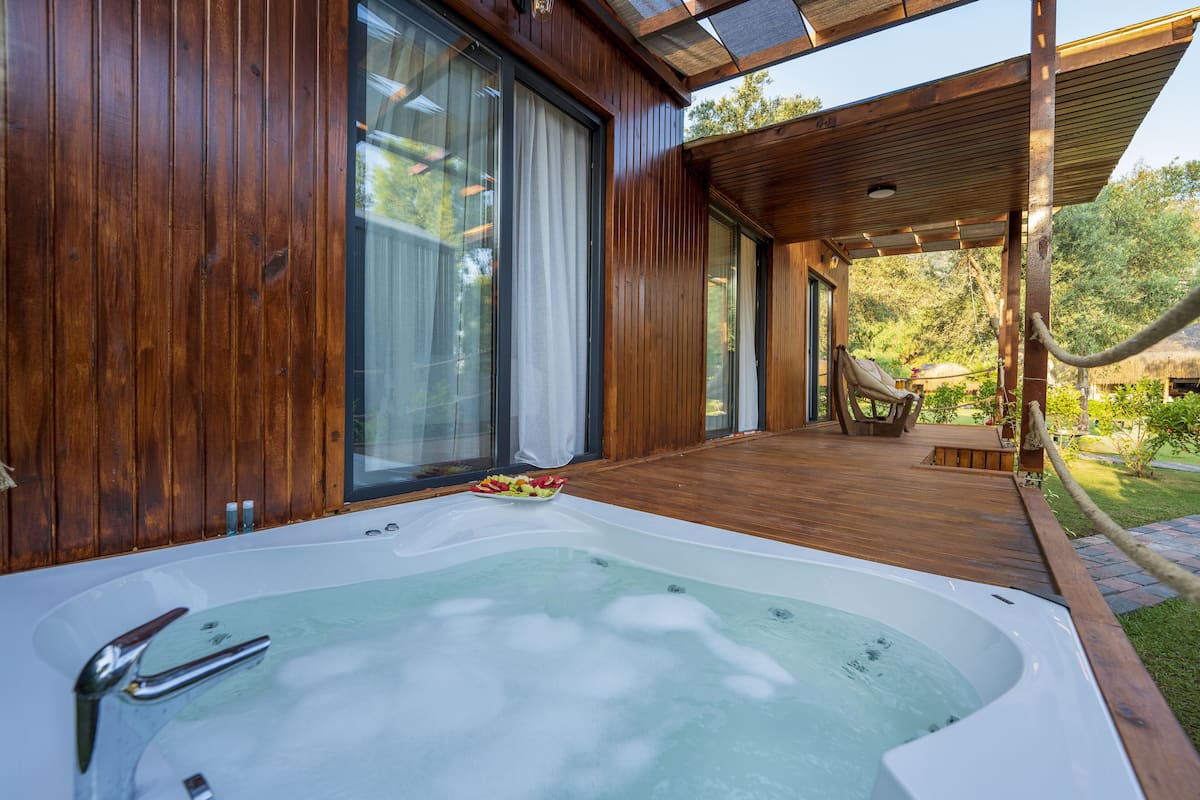 Eine Holzterrasse mit Whirlpool, großen Schiebegläsern und einer überdachten Sitzgelegenheit.