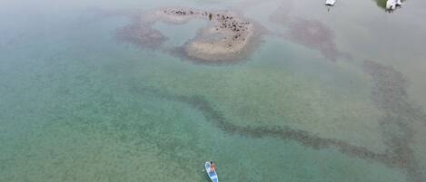 An aerial view of a beach with clear waters, a small island, and a boat.