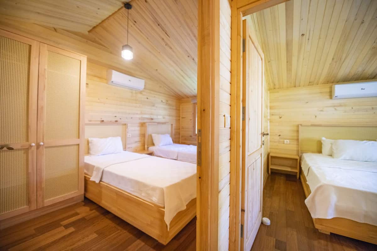 Eine Holzhütte mit zwei Schlafzimmern, jeweils mit einem Bett und einem Nachttisch. Es gibt eine Holztür mit einem Moskitonetz und eine Wandklimaanlage.