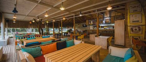 A wooden deck with benches and tables, a kitchen area, and a surfboard with text.