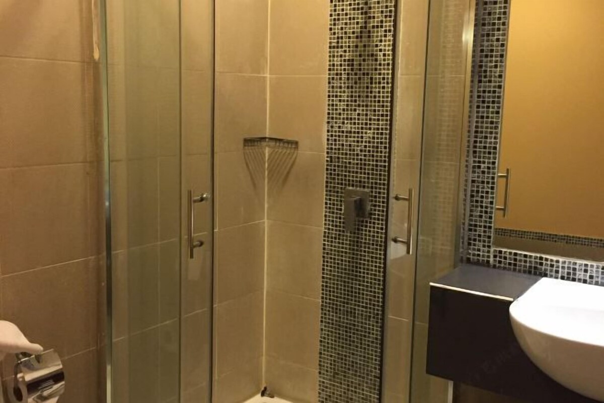 A bathroom with a glass shower enclosure, a tiled wall with a mosaic pattern, and a sink with a dark countertop.