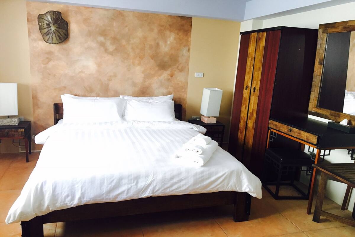 A neatly made bed with white linens and pillows, a wooden nightstand with a lamp, and a wooden cabinet with a mirror.