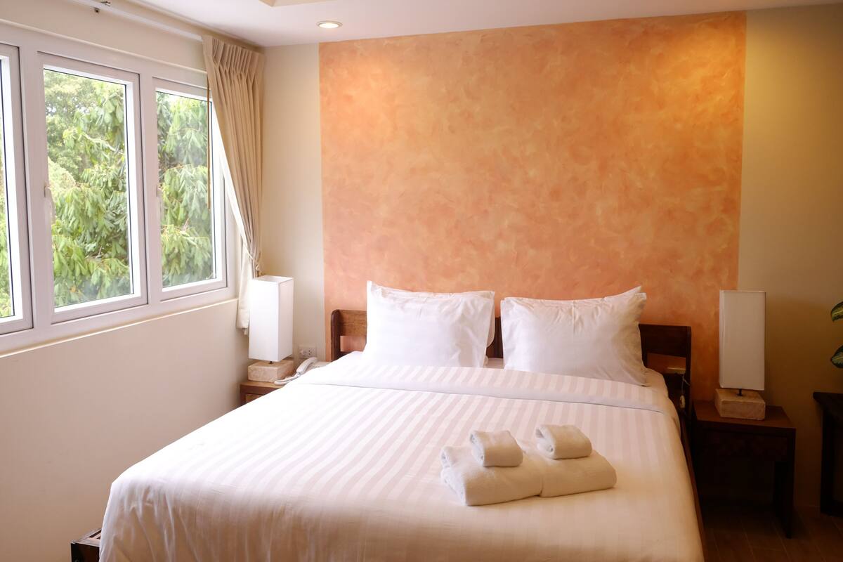 A hotel room with a large bed, two bedside tables, a nightstand, and a window with curtains.
