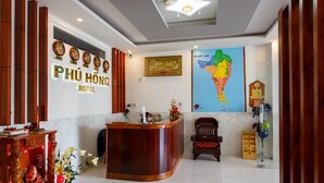 A hotel reception area with a wooden reception desk, a large map on the wall, and a traditional decorative piece on the left. - Phu Hong Hotel (Phu Quoc)