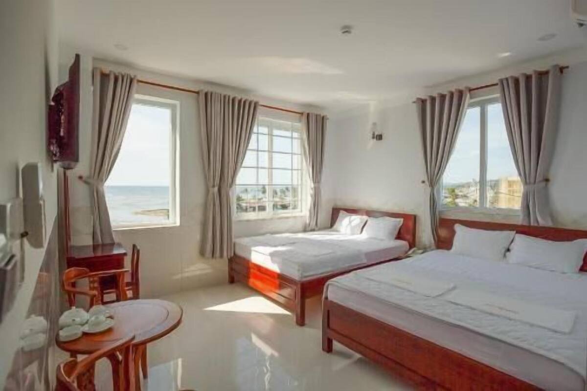 A hotel room with two beds, a TV, a small table with plates, and large windows with curtains.