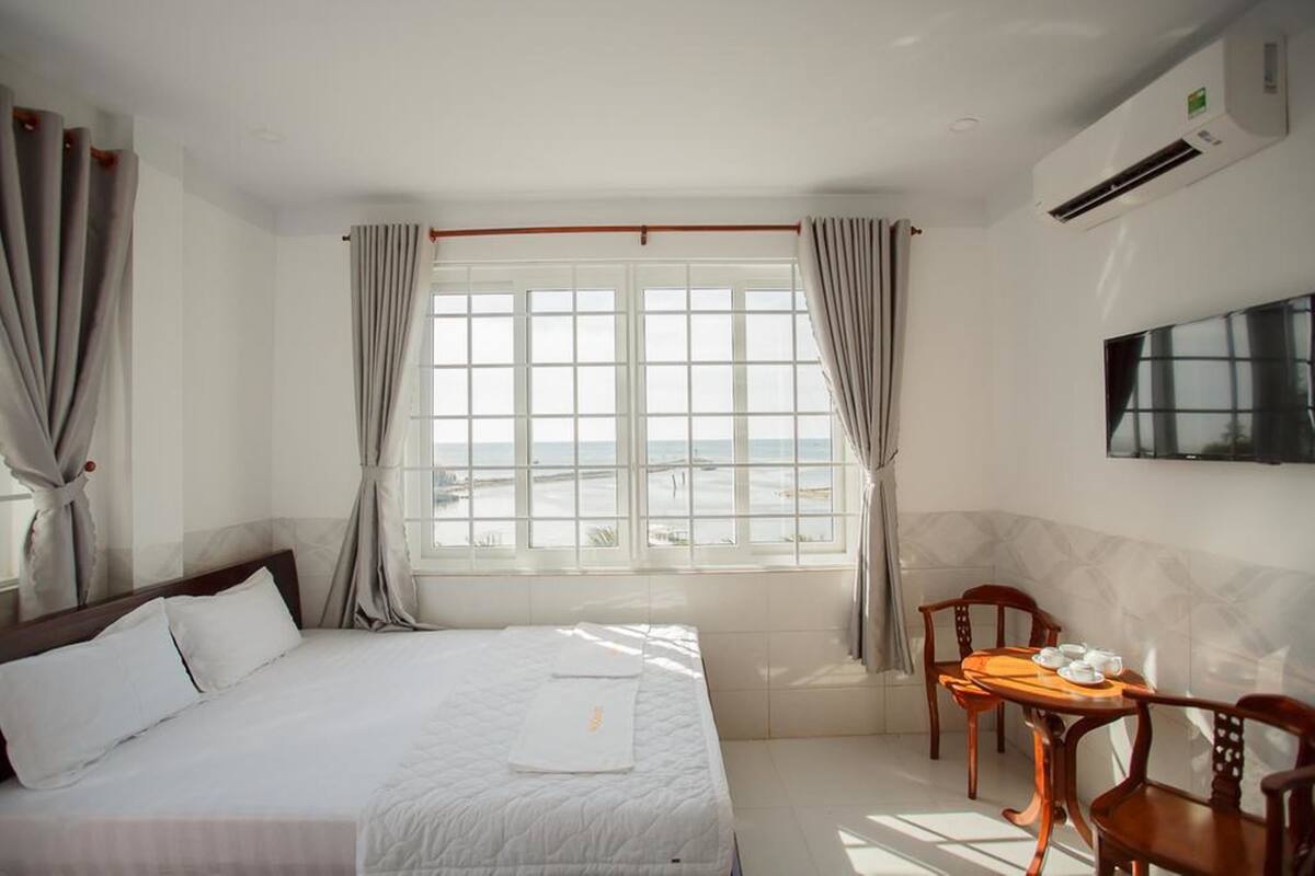 A hotel room with a bed, a dining table with chairs, a TV, and a window with curtains.