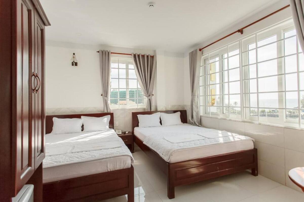 A hotel room with two beds, a large window with curtains, and a view of the city.