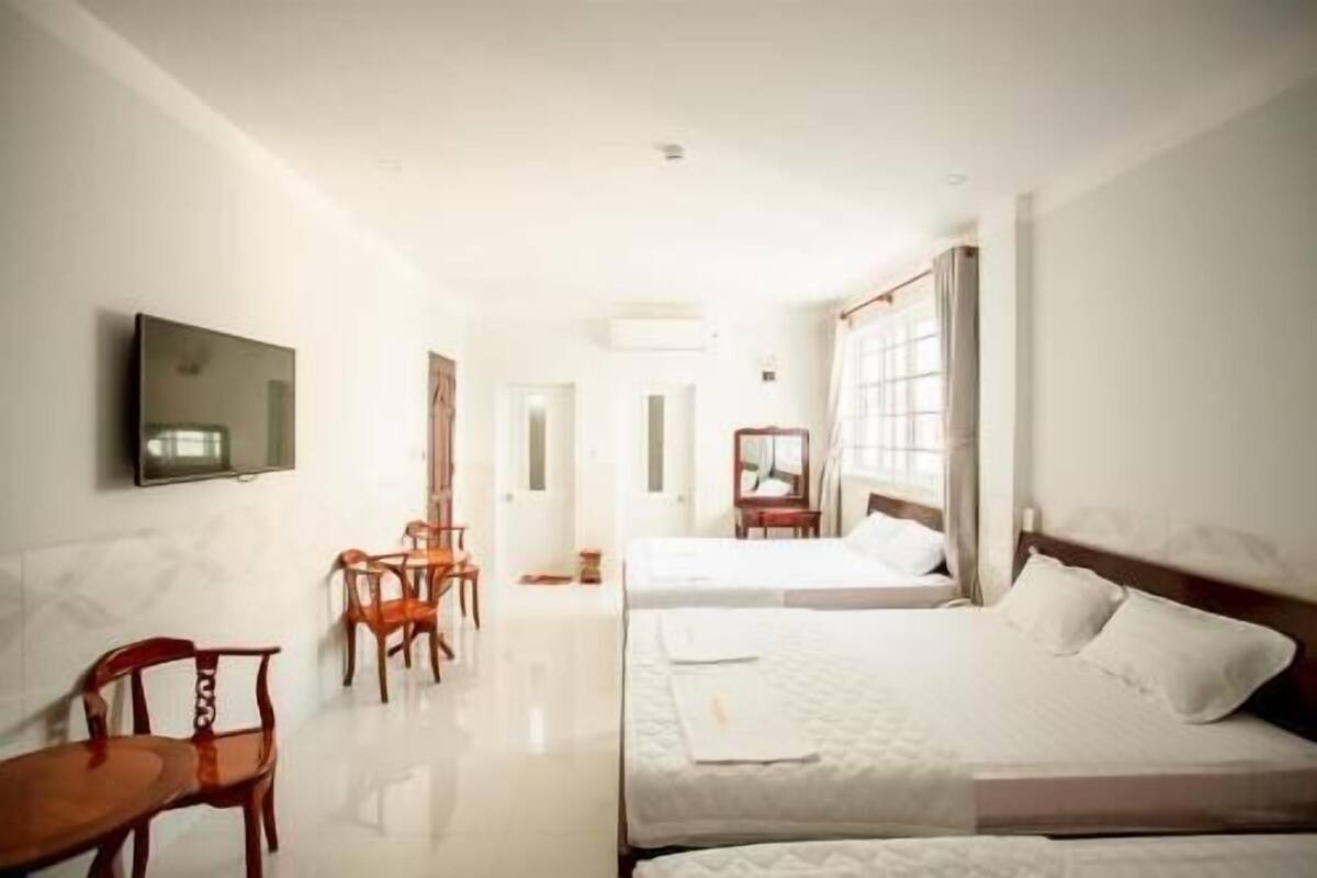 A hotel room with two beds, a TV, a desk with a chair, and a window with curtains.