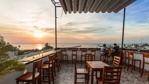 A terrace with wooden tables and chairs, overlooking a coastal view with boats and a sunset. - Phu Hong Hotel (Phu Quoc)