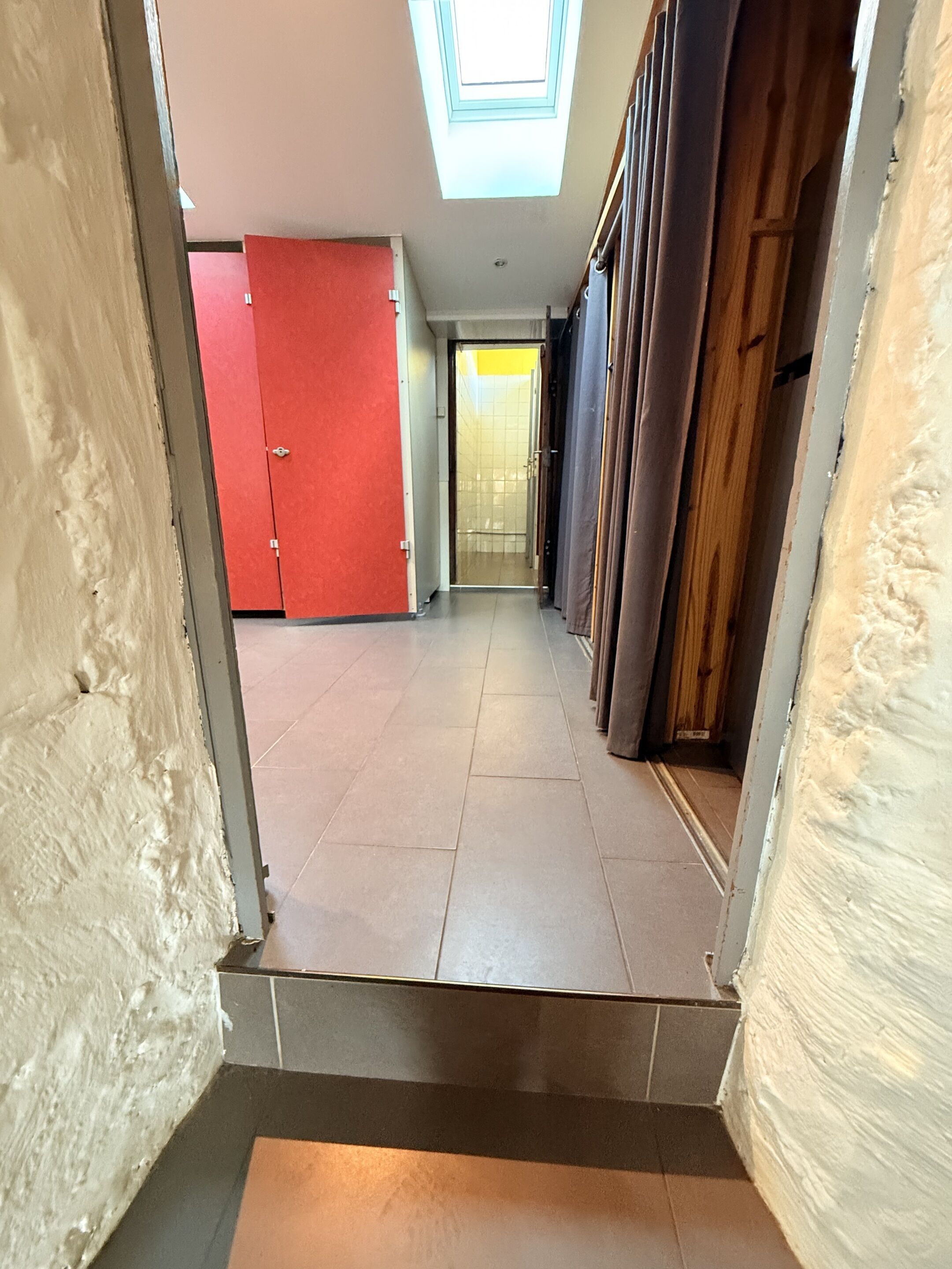 A hallway with a skylight, red doors, and a tiled floor.