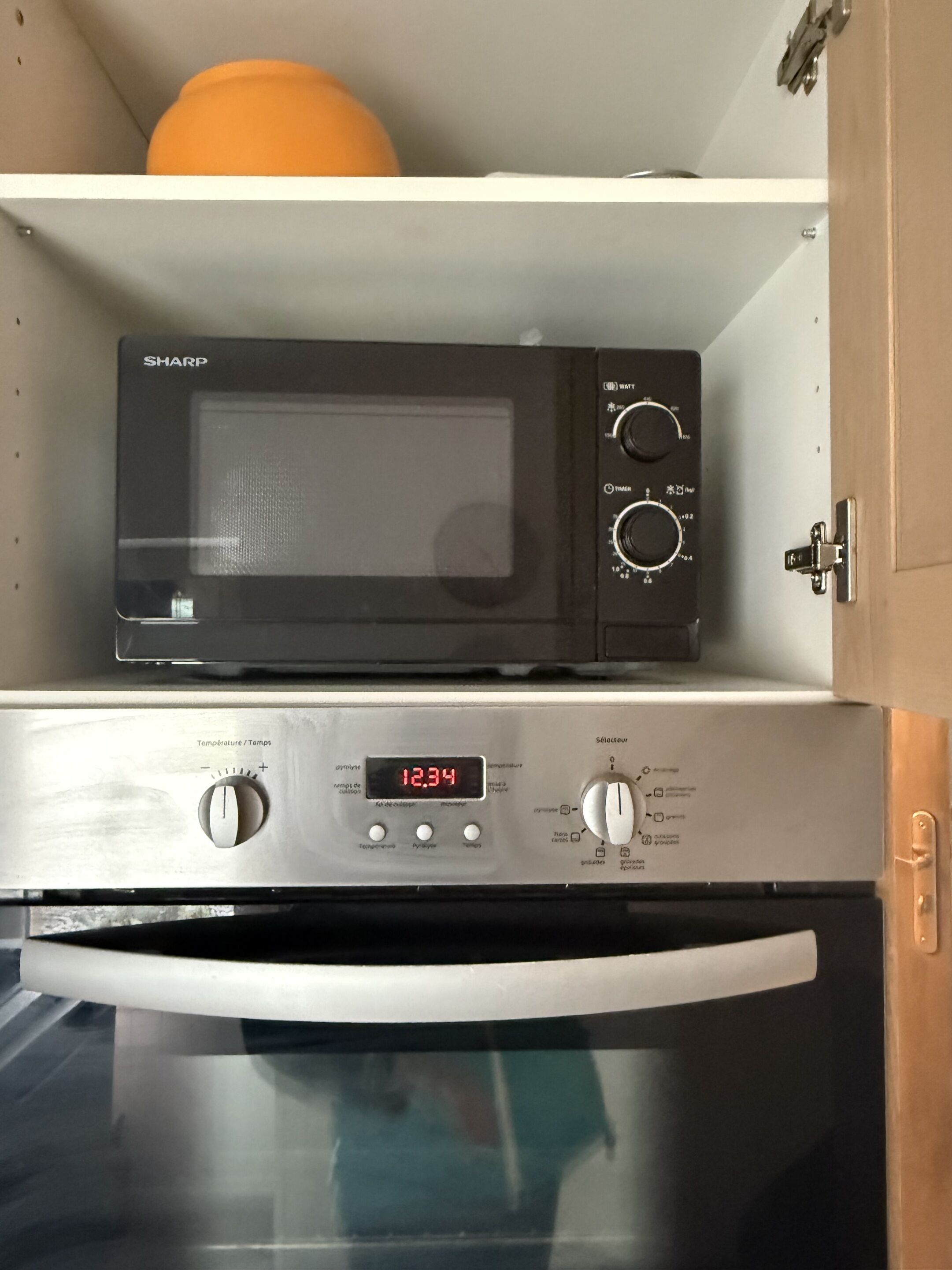 A kitchen with a microwave on a shelf above a stainless steel oven.