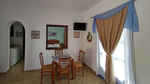 Un comedor con una mesa redonda, cuatro sillas de madera, un espejo y un televisor en la pared.