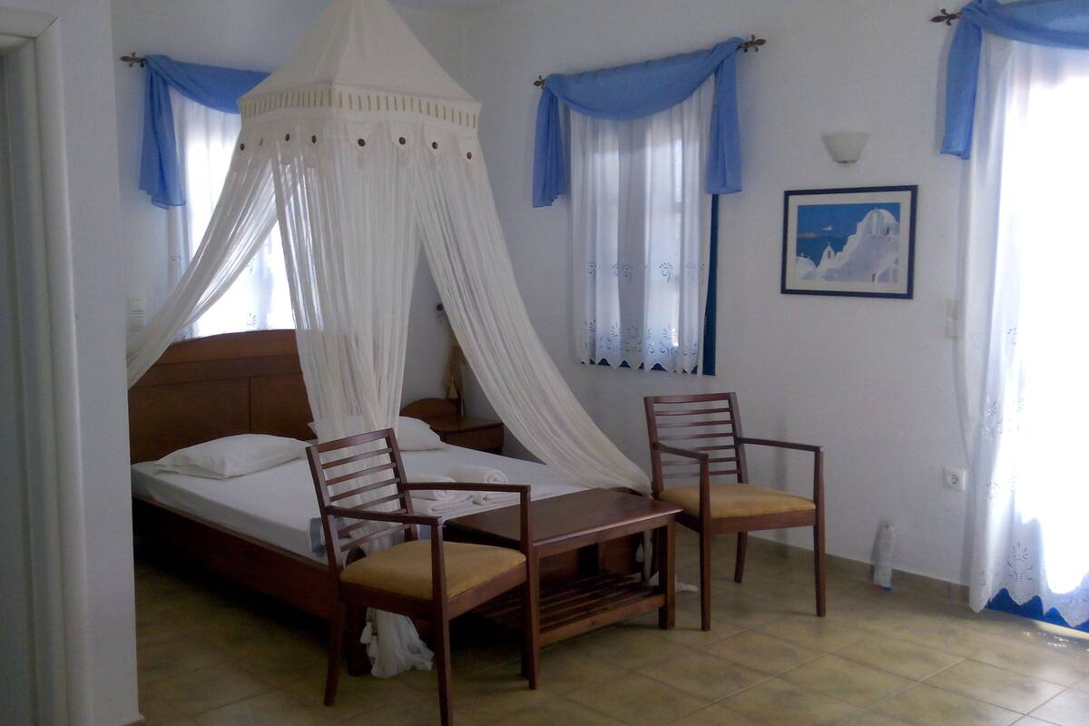 A bedroom with a bed, two chairs, a nightstand, and a window with curtains.