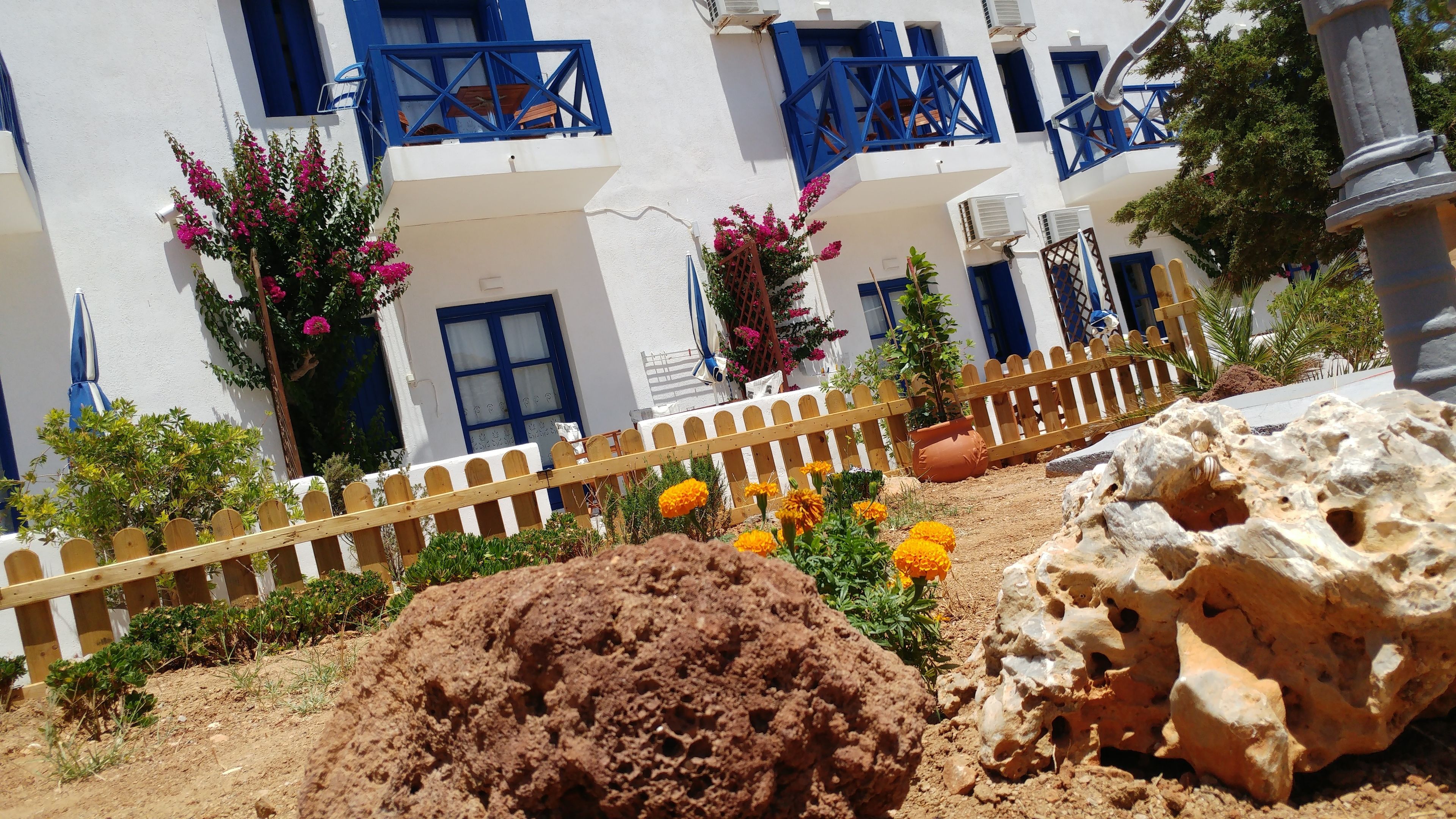 A building with white walls and blue shutters, a wooden fence, and a rock with holes.