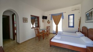 Un dormitorio con cama, escritorio y silla. Hay un televisor en la pared y una ventana con cortinas.